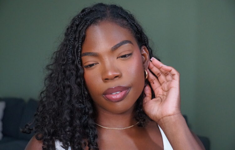 Woman with braids wearing soft glam makeup and glossy lips, looking off to the side