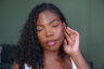 Woman with braids wearing soft glam makeup and glossy lips, looking off to the side